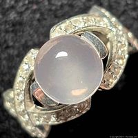 Close-up front view of the ring showing the round rose quartz gemstone and clear accent stones in the sterling silver band.