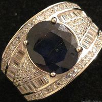 Front view of men's silver rhodium plated ring with large round dark blue sapphire and clear accent stones.