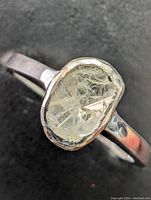 Close-up of the ring showing the flat diamond's rough and lattice style with inclusions.