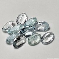 Top angled view showing all faceted aquamarine gemstones piled together on a white surface, highlighting various cuts.