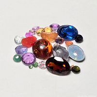 Multiple assorted genuine loose gemstones of various colors and cuts displayed on white background