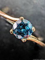 Close-up of round blue diamond in six-prong 10k yellow gold setting on polished band