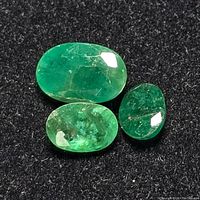 Three oval emerald gemstones placed on black background showing color and inclusions