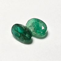 Two oval emerald stones on white background showing color and clarity differences