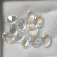 Top view of 11 faceted oval moonstone gemstones showing blue sheen and translucency on a gray background.