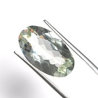 Close-up view of an oval faceted green amethyst gemstone held by tweezers showing transparency and cut details.