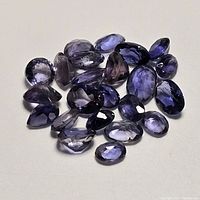 Photo showing 21 loose faceted iolite gemstones in various sizes and shapes, primarily oval and marquise.
