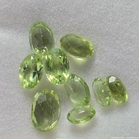 Nine loose faceted peridot stones in a white cushioned display showing their light green color and transparency.