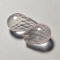 Photo showing two faceted rose quartz teardrop gemstones side by side with light pink translucent appearance and checkerboard faceting.