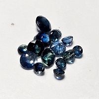 Multiple loose faceted sapphire gemstones of various cuts and sizes shown against a white background.