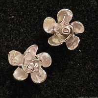 Pair of silver earrings with flower-shaped design, showing the front top view of both earrings on a black background.