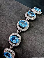 Close-up of sterling silver bracelet featuring five oval-shaped blue topaz gemstones surrounded by halo of clear stones.