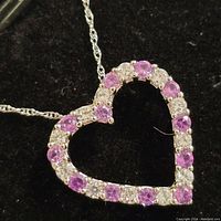 Close-up image of a sterling silver heart-shaped necklace pendant with alternating purple and clear cubic zirconia stones on a twisted silver chain.
