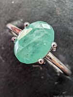 Close-up image showing oval-shaped emerald stone set in sterling silver ring, highlighting the stone and prong setting.