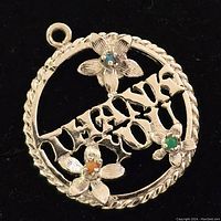 Front view of the round sterling silver pendant showing the inscribed 'THANK YOU' and three flowers with colored stones in blue, orange, and green.