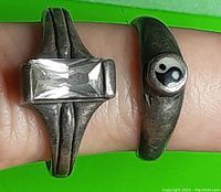 Two .925 stamped sterling silver rings on finger: one set with a rectangular clear stone and the other open-ended with a Yin Yang symbol