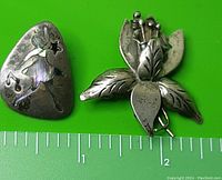 Both brooches side by side on a green background with ruler for size reference.