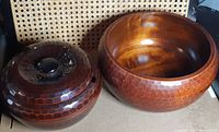 Two wooden bowls side by side. Smaller bowl has a lid and is darker with honeycomb texture, larger bowl without lid and lighter color with same texture.