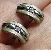 Close-up photo of the two curved sterling silver earrings with pink stones set in the center, held in a hand.