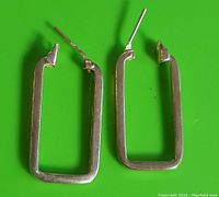 Pair of rectangular hoop earrings displayed on a green background, showing their shape and overall condition.