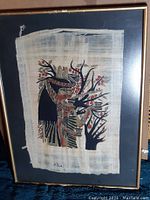 Framed Egyptian papyrus artwork featuring a traditional figure in profile with black trees and red accents on natural papyrus material.