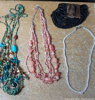 Four pieces of jewelry laid out on a wooden surface: three necklaces and one bracelet as described.