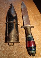 Cutting tool with decorative sheath standing upright on a surface, showing blade details and handle colors.