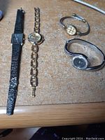 Four quartz watches displayed on a surface showing different bracelets and dial shapes.