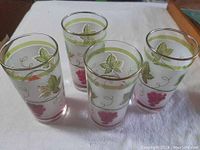 Four clear glass frosted tumblers with red grapes, green leaves, vines and gold rim