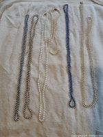 Full view of six glass pearl necklaces showing various colors and lengths laid side by side on a light fabric background.