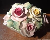 Close-up photo of porcelain floral arrangement showing pink, white, and yellow roses with green leaves and some minor wear.