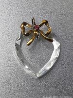Heart-shaped clear faceted pendant with sterling silver bow holding a red or pink stone, shown against gray background.