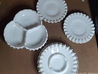Top view showing the four milk glass pieces: two small scalloped plates, one divided dish with three sections, and one hobnail pattern ashtray.