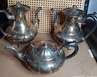 Photo showing two identical taller silver plated tea pots and one shorter squatter tea pot all with lobed body designs and curved spouts