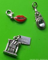 Three sterling silver items including a red lips charm with lobster clasp, an ornate pendant with clear faceted stone, and a small silver charm of a rocking chair with a tag reading 'STERLING CAMPBELL'.