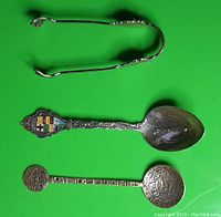 View of two tiny forks and one decorated spoon with colorful emblem and engraved design on green background