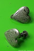 Pair of sterling silver heart-shaped clip-on earrings with engraved designs on a green background, display of both earrings with visible screw hinge clip-on mechanism