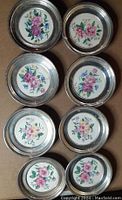 Eight coasters arranged in two columns showing top view of floral inserts and silver frames