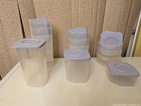 Photo showing three different sizes of Tupperware Fresh N Cool containers with purple lids arranged on a surface, each size has four containers stacked behind the others.