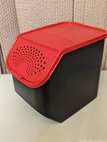 Front angled view of the black rectangular Tupperware Potato Keeper with its red ventilated lid closed.