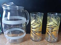 Two Libbey tall glasses with gold wheat pattern and glass jug with white bands.