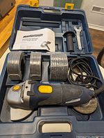 Mastercraft angle grinder with four discs, side handle, wrench, and manual in blue plastic case.