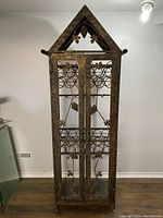 Front view of iron wine cabinet closed showing grape leaf design on glass doors and peaked top