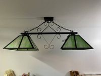 Wide view of green ceiling light fixture with two pyramid-shaped green stained glass lamp shades, mounted with black metal chains and decorative elements.