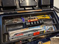 Open toolbox showing drill bits, a yellow utility knife, and other small hand tools in the top compartment