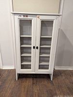 Front view of the white wooden cupboard showing two glass doors and internal shelving.
