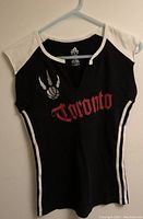 Black Adidas Toronto Raptors shirt hung on a hanger, front view showing 'Toronto' text and basketball claw logo.