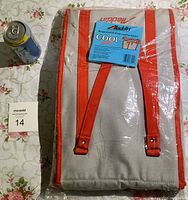 Full view of the Aladdin Cool Bag in packaging showing beige fabric with red trim and handles, unopened with product label attached.