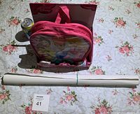 Photo showing the pink Disney Princess themed game pack with a roll of wrapping paper and a soda can for size perspective on a floral tablecloth.