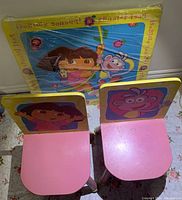 View of two pink seats with Dora and Boots graphics on chair backs and the wrapped table with Dora and Boots on top.